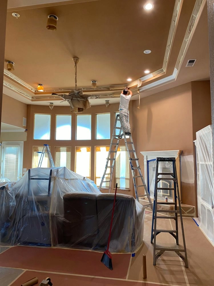 Interior painter on a ladder applying finish to a detailed ceiling in a Fresno home